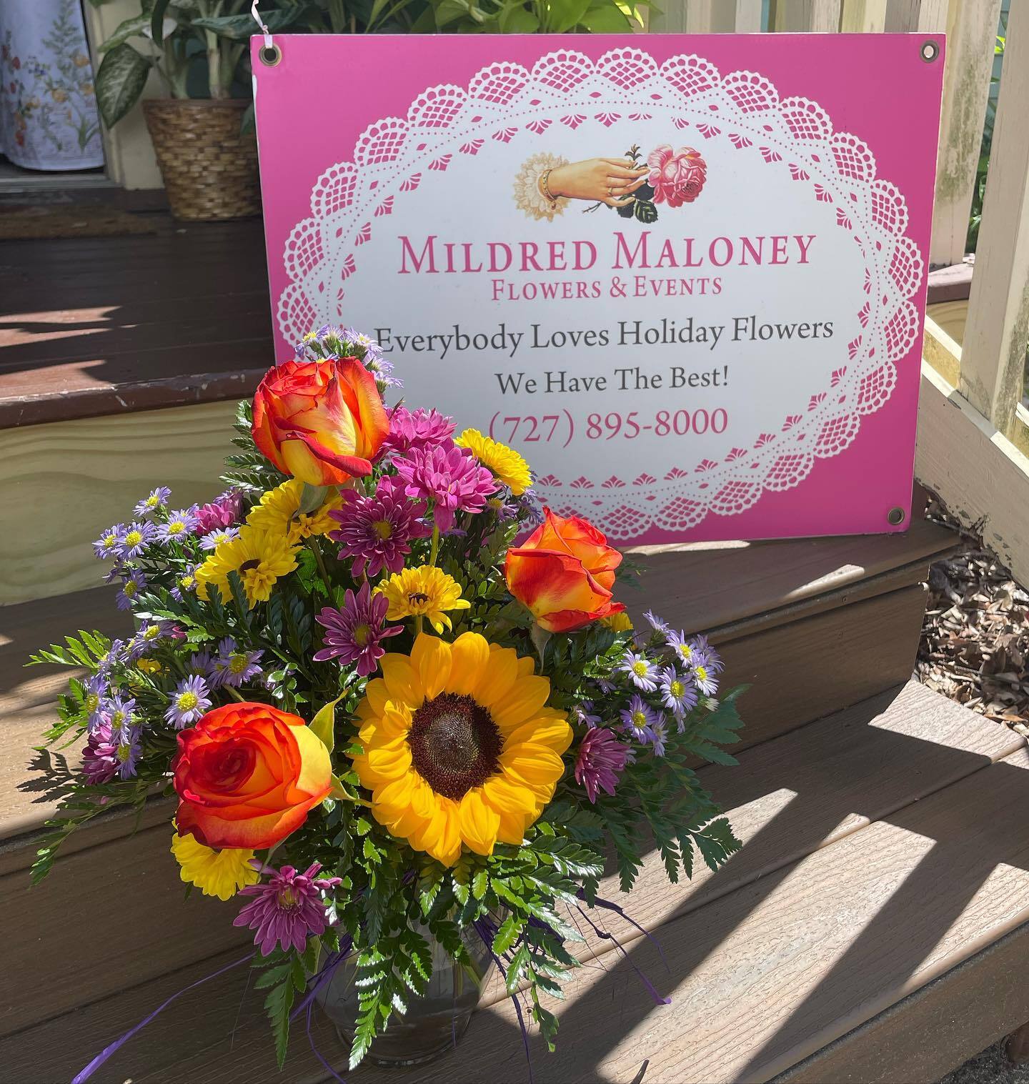 Mildred Maloney Flowers sign beside a bright sunflower and rose bouquet